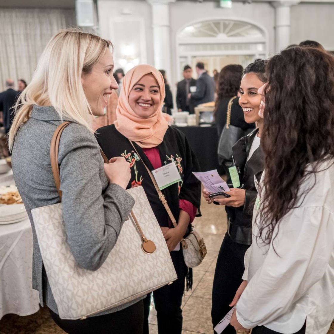 a group of women stand smiling and talking to eachother at a reception