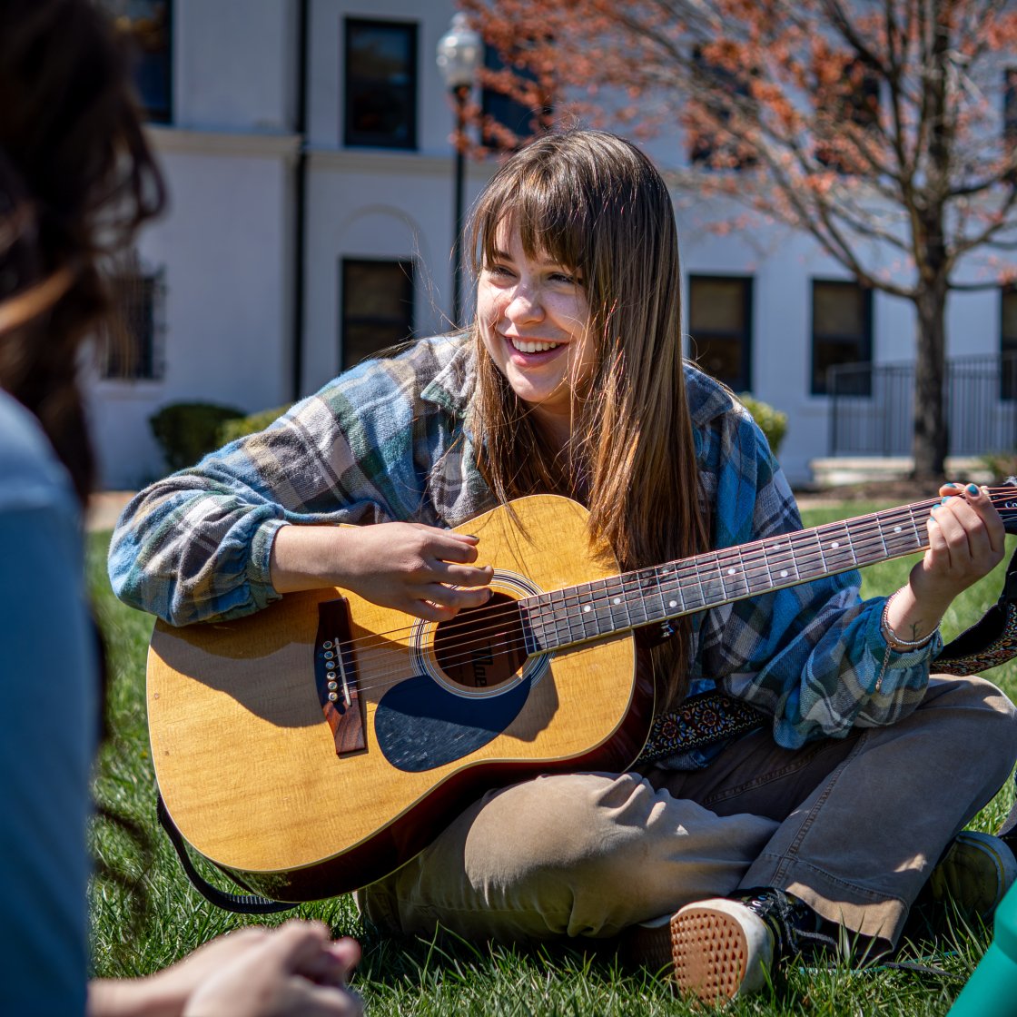 student playing guitar outside on the grass