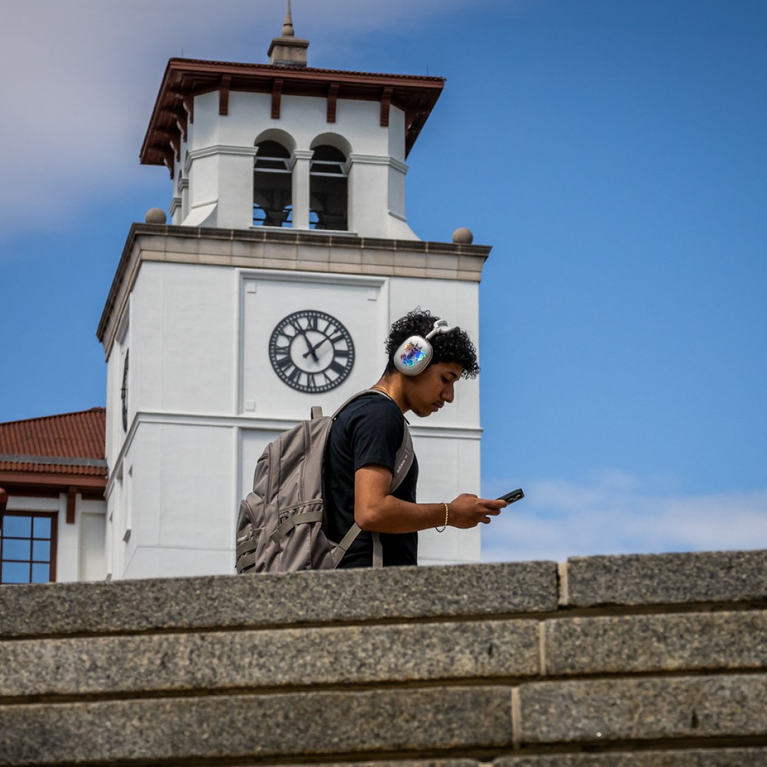 A student wearing headphones on his phone 