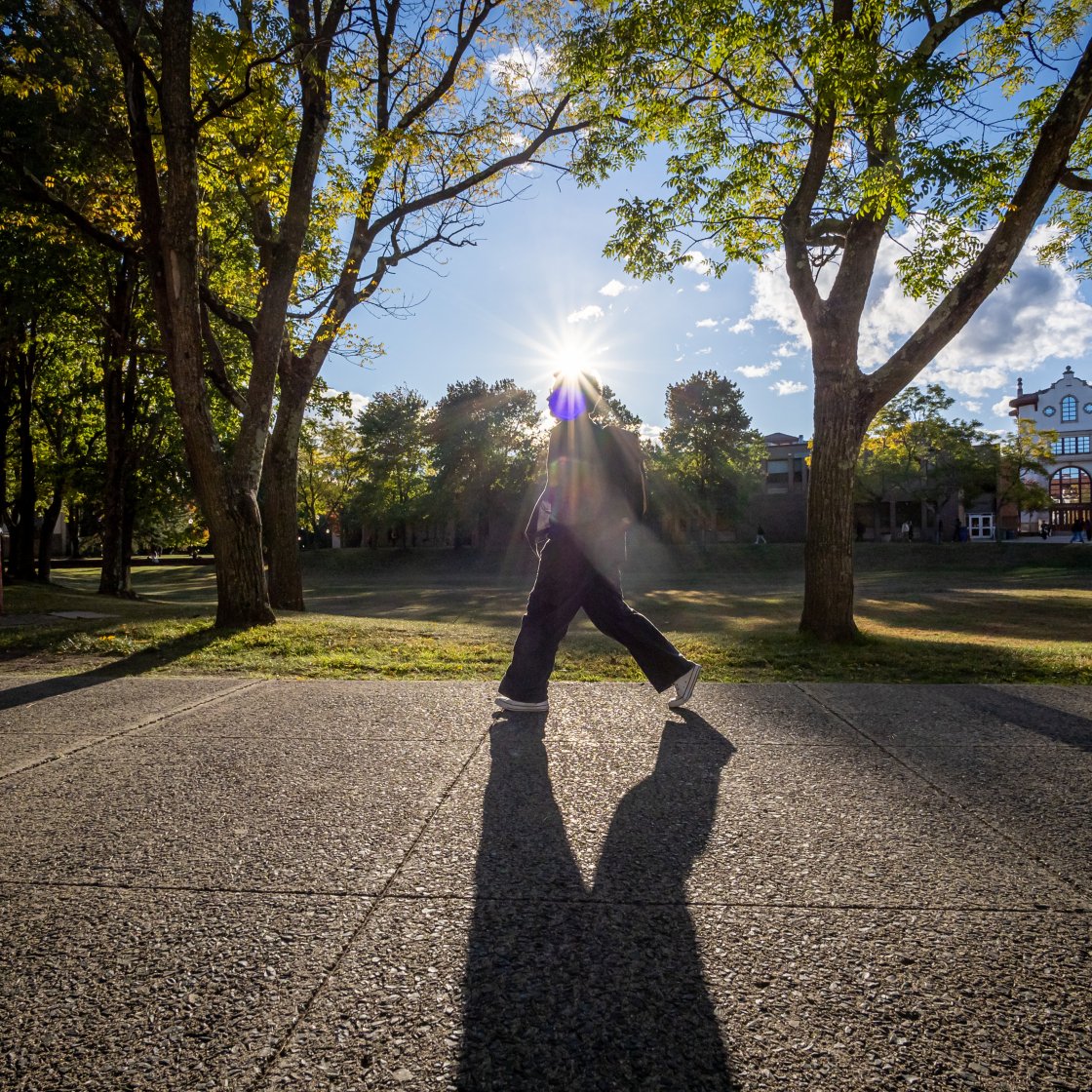 student walking with sun behind them casting a shadow