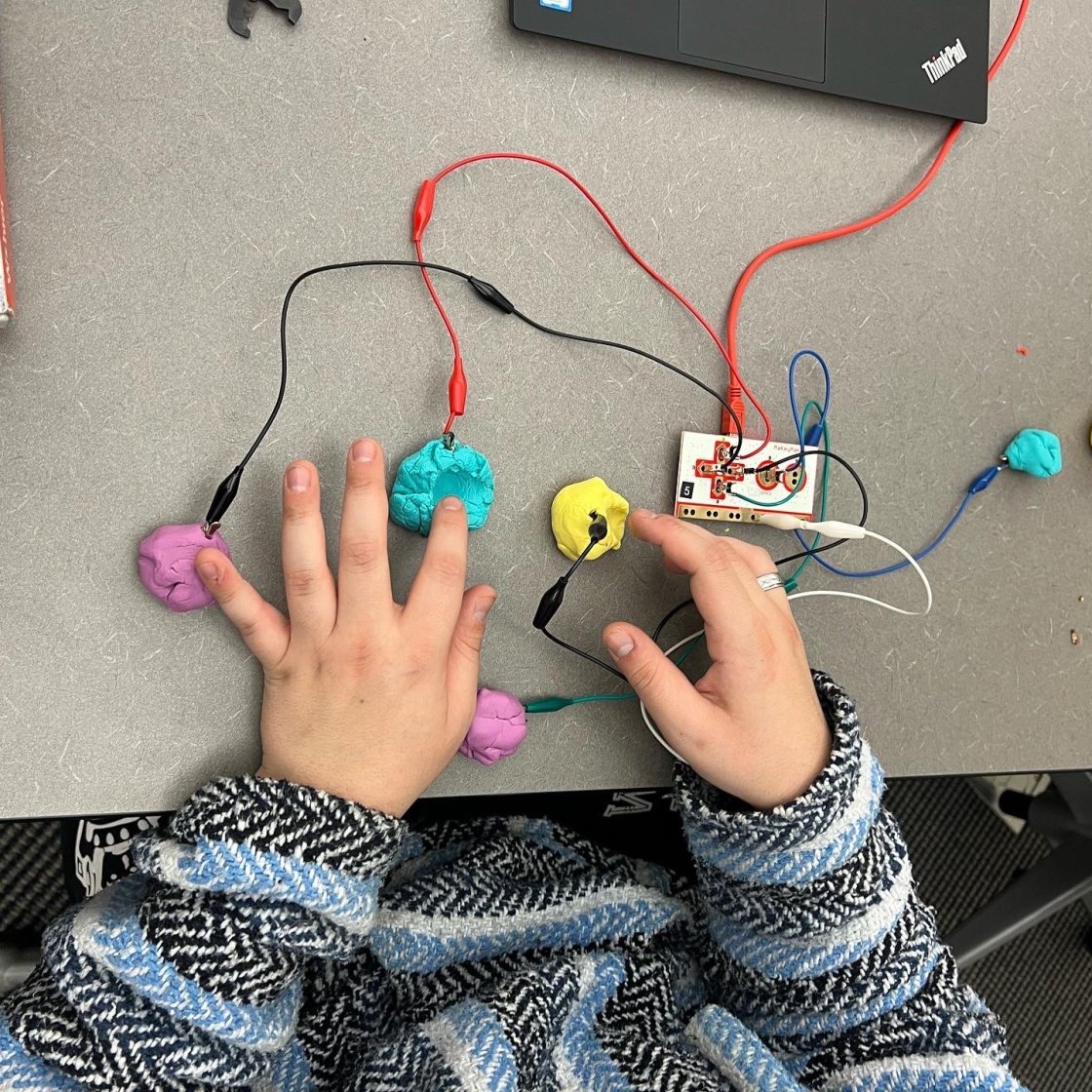 Hands touching putty with wires connected 