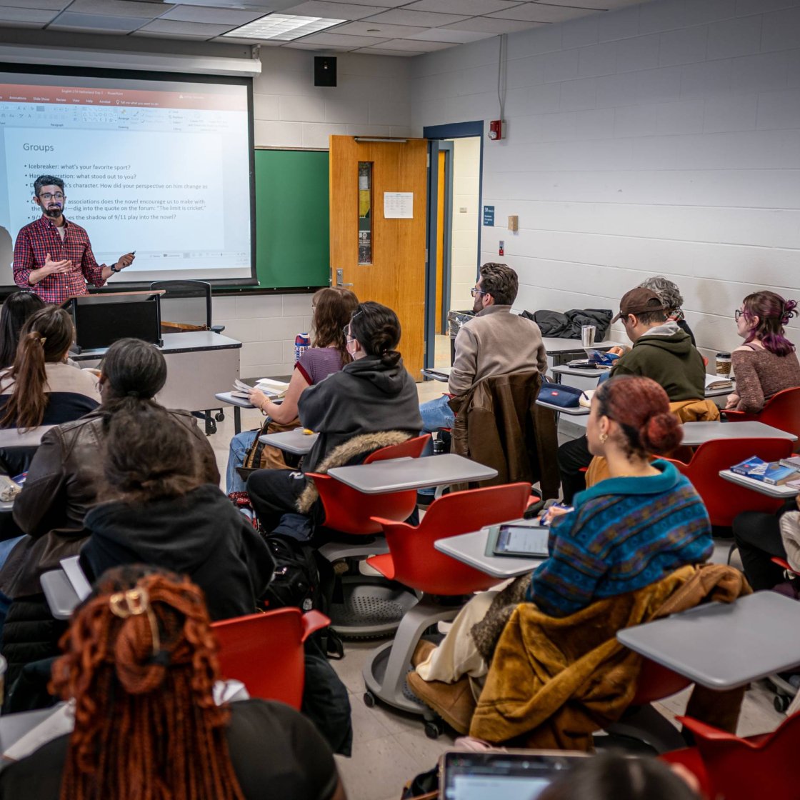 A college professor stands at the front of his class and presents a lesson to a classroom full of students