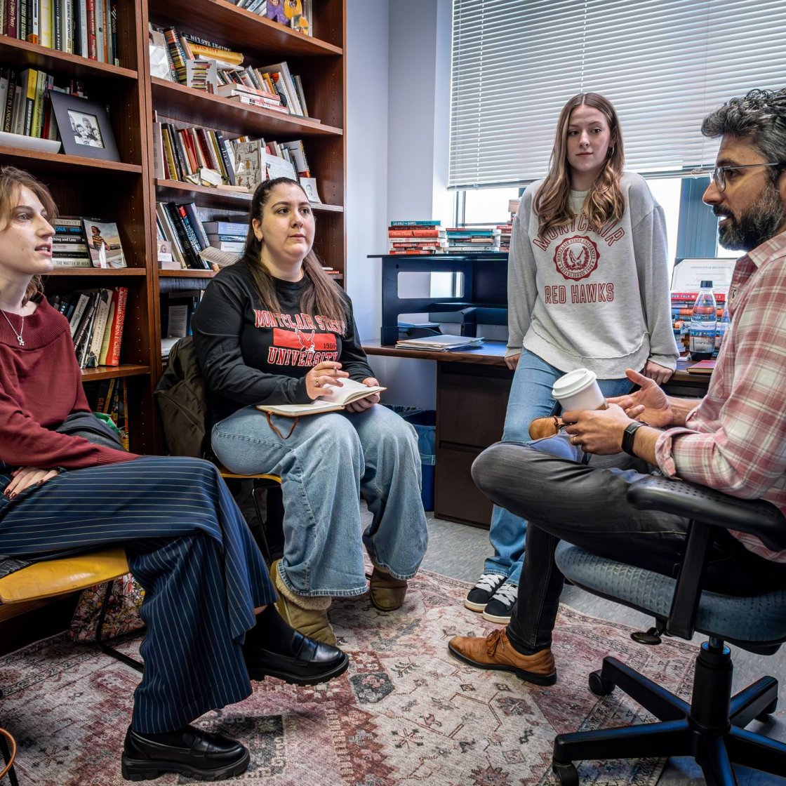 A college professor meets with three students in his office.