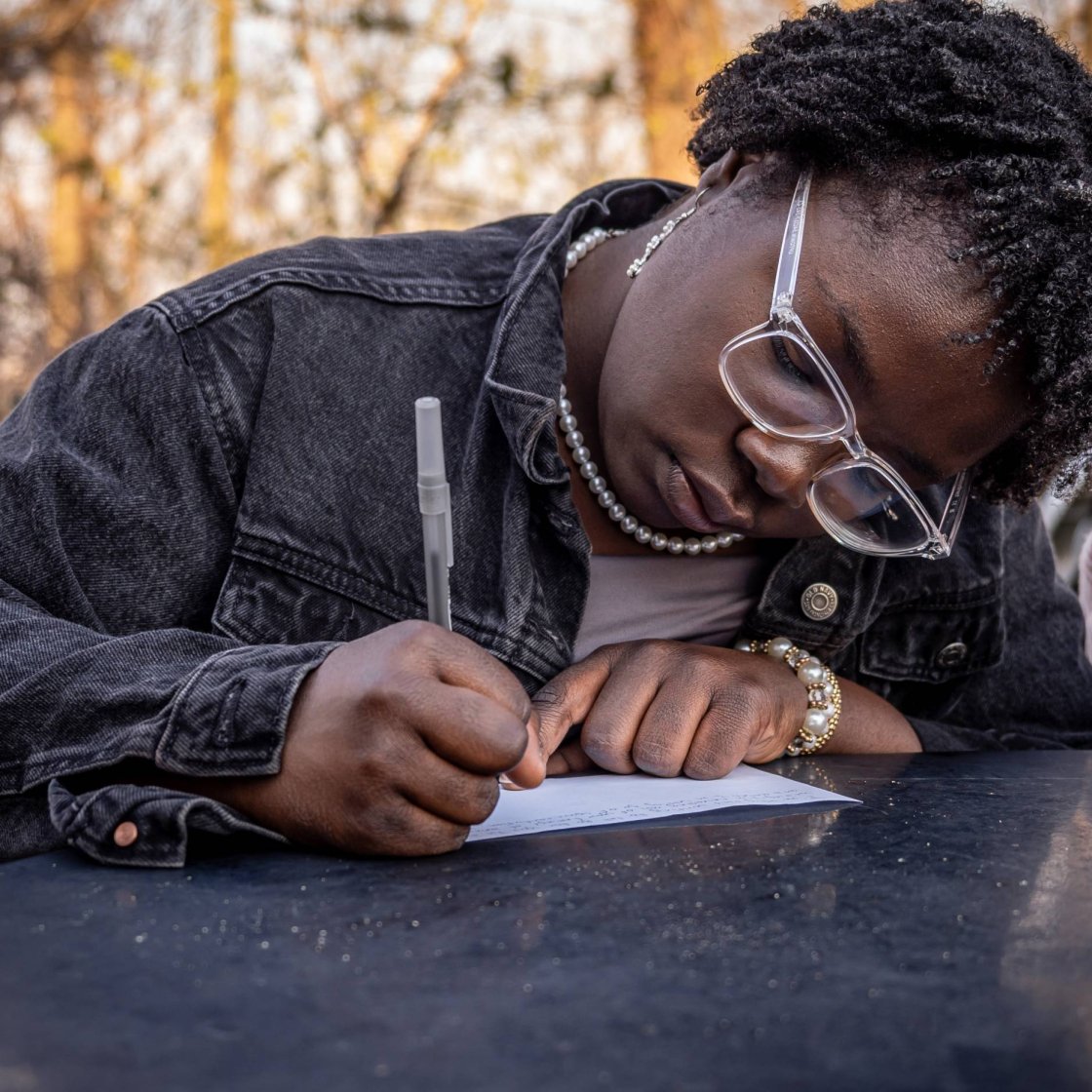 A student leaning over a table, writing with a pen on a piece of paper