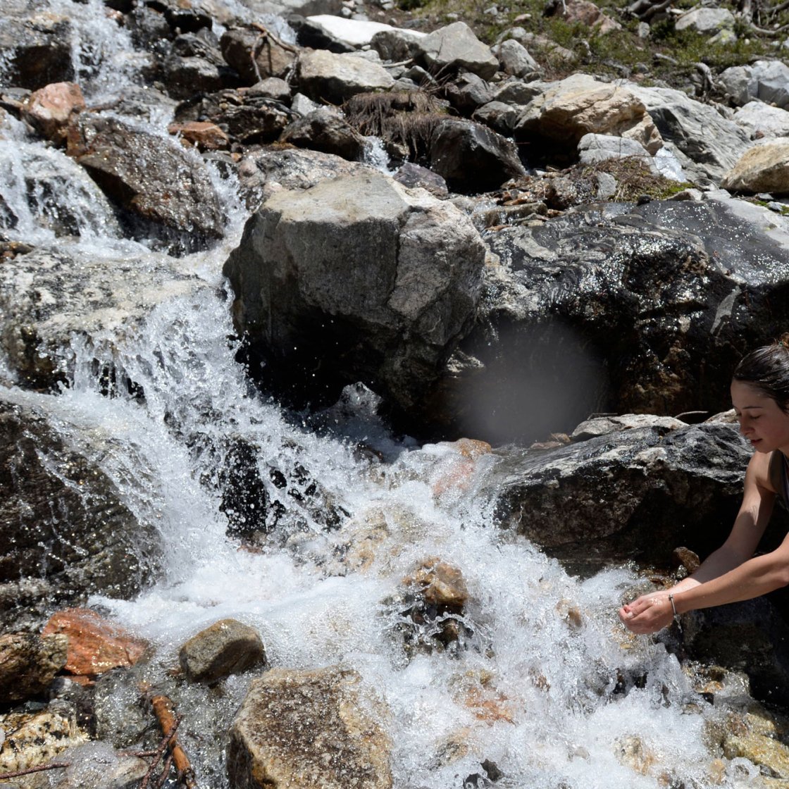 student on class hike getting water from a rushing stream