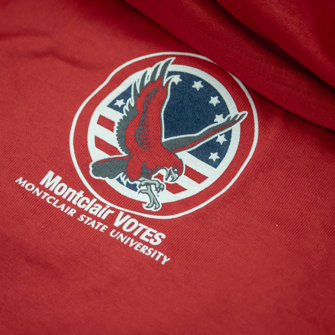 Close-up of a red Montclair State University “Montclair Votes” shirt featuring an eagle logo and patriotic design.