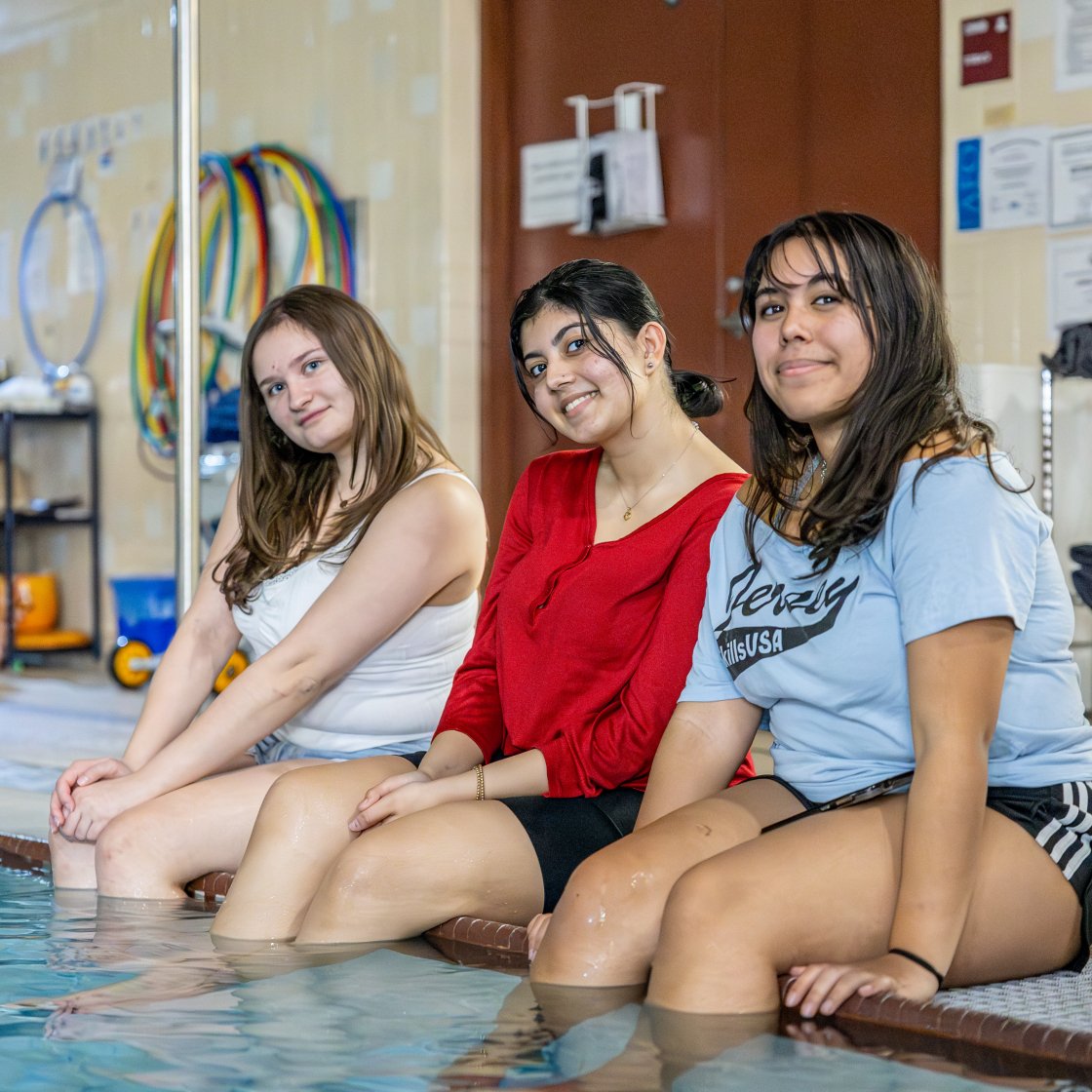 three students sitting on the side of the pool