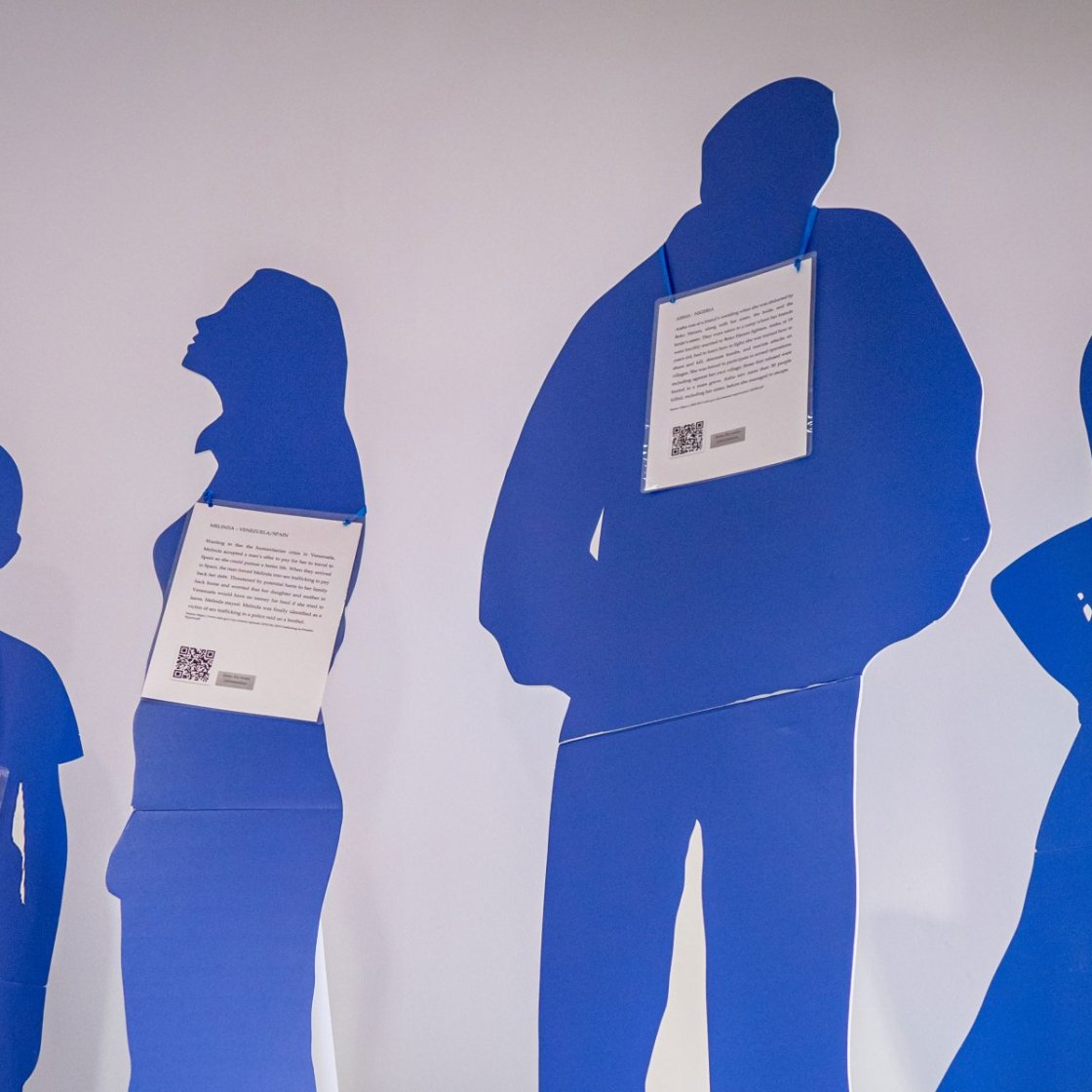 A collection of blue cardboard cutout people wearing paper signs with details about human trafficking