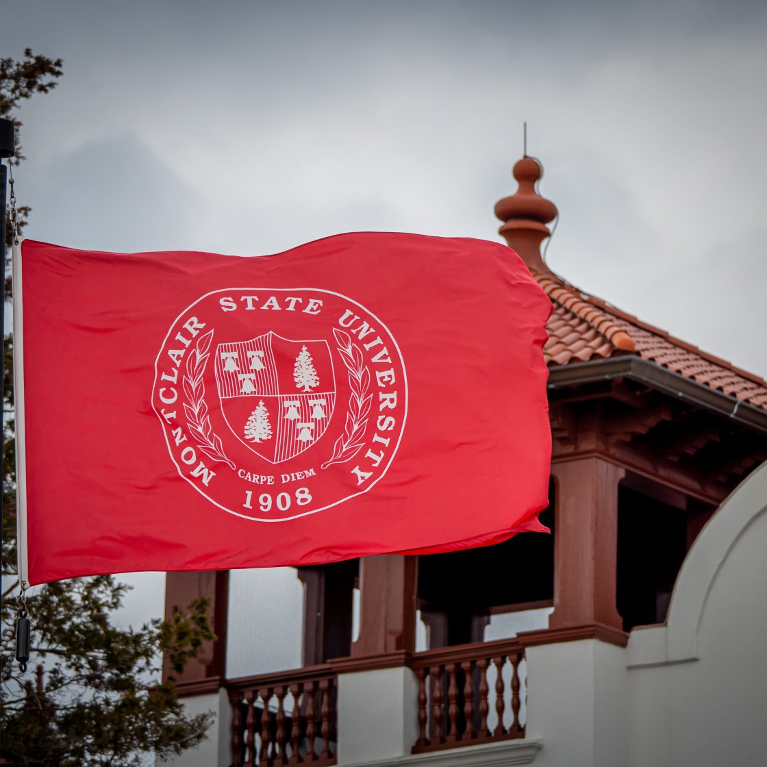 Montclair State University flag - red background with white seal - flying on flagpole