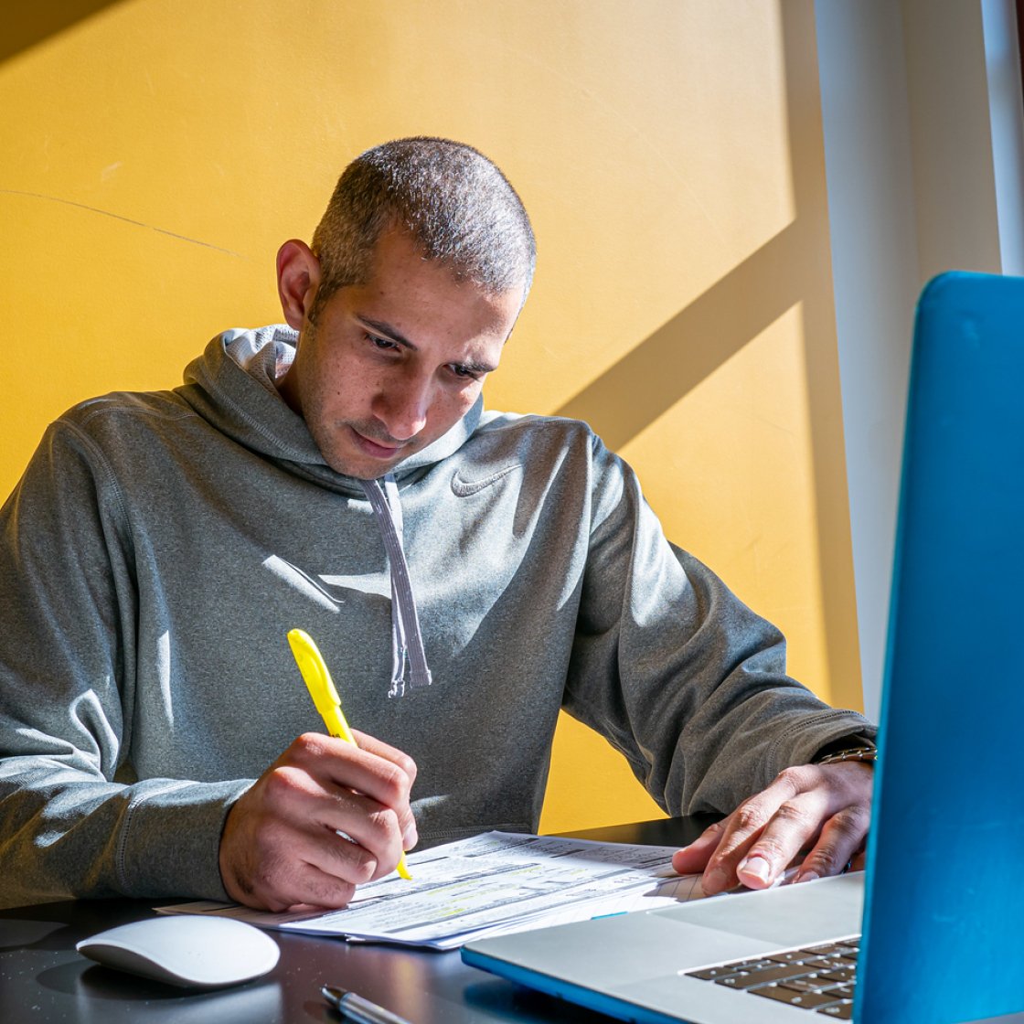 Student wearing a hoodie sitting in front of his laptop highlighting notes.