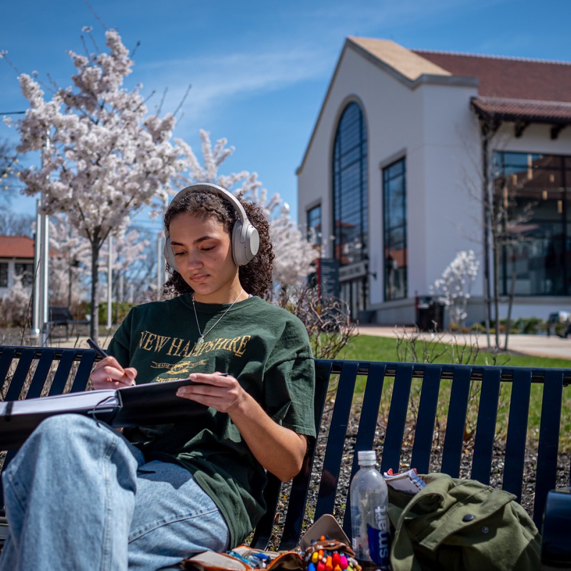 Student wearing headphones draws in her notebook while sitting outside Cole Hall in the spring.