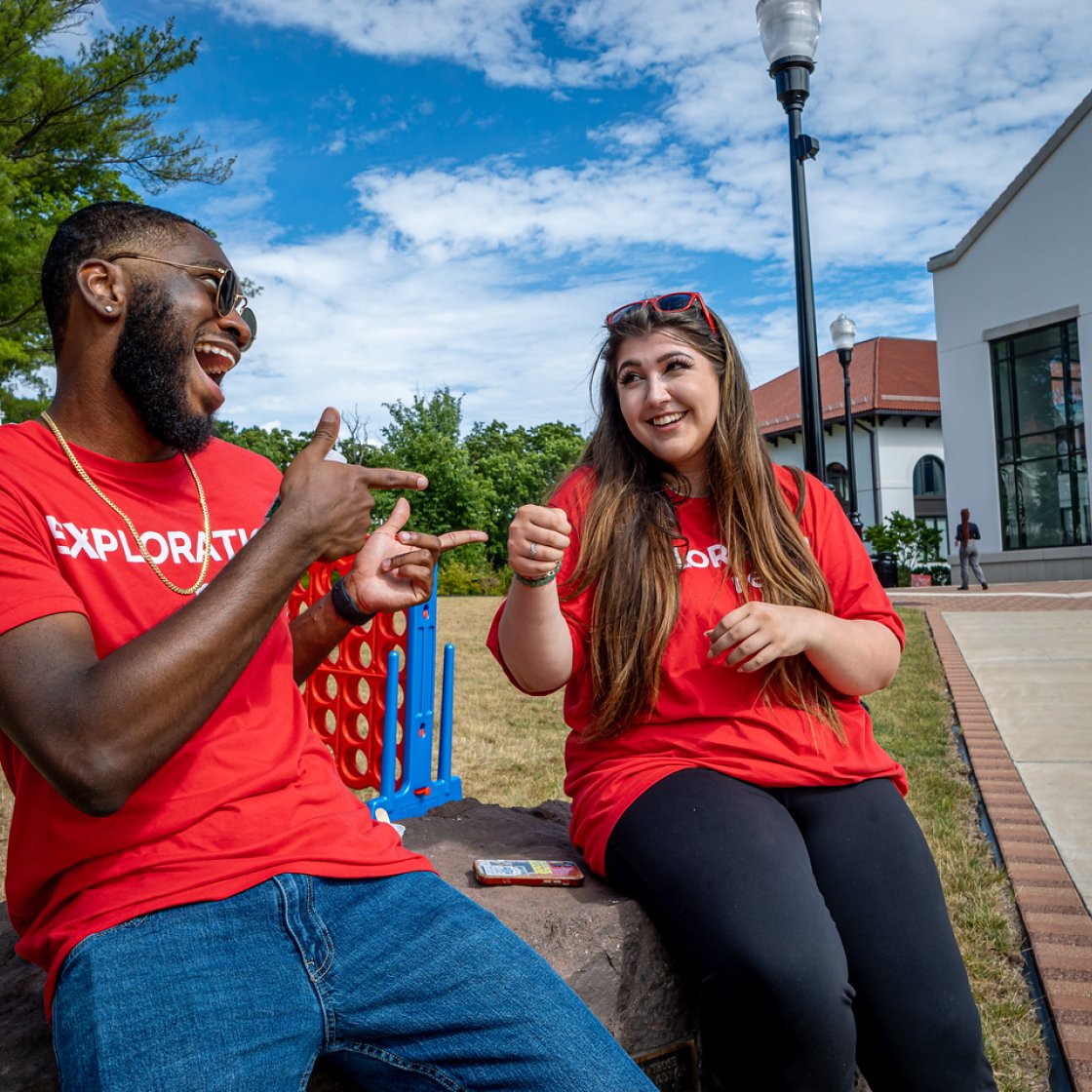 Two students wearing red Exploration Ready tees laughing outside Cole Hall in the summer.