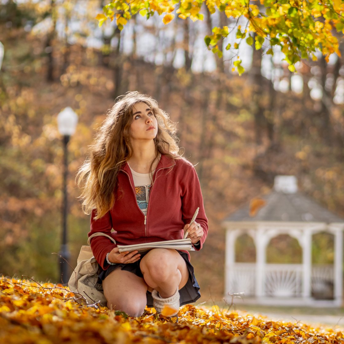 student sitting outside during the fall looking upward