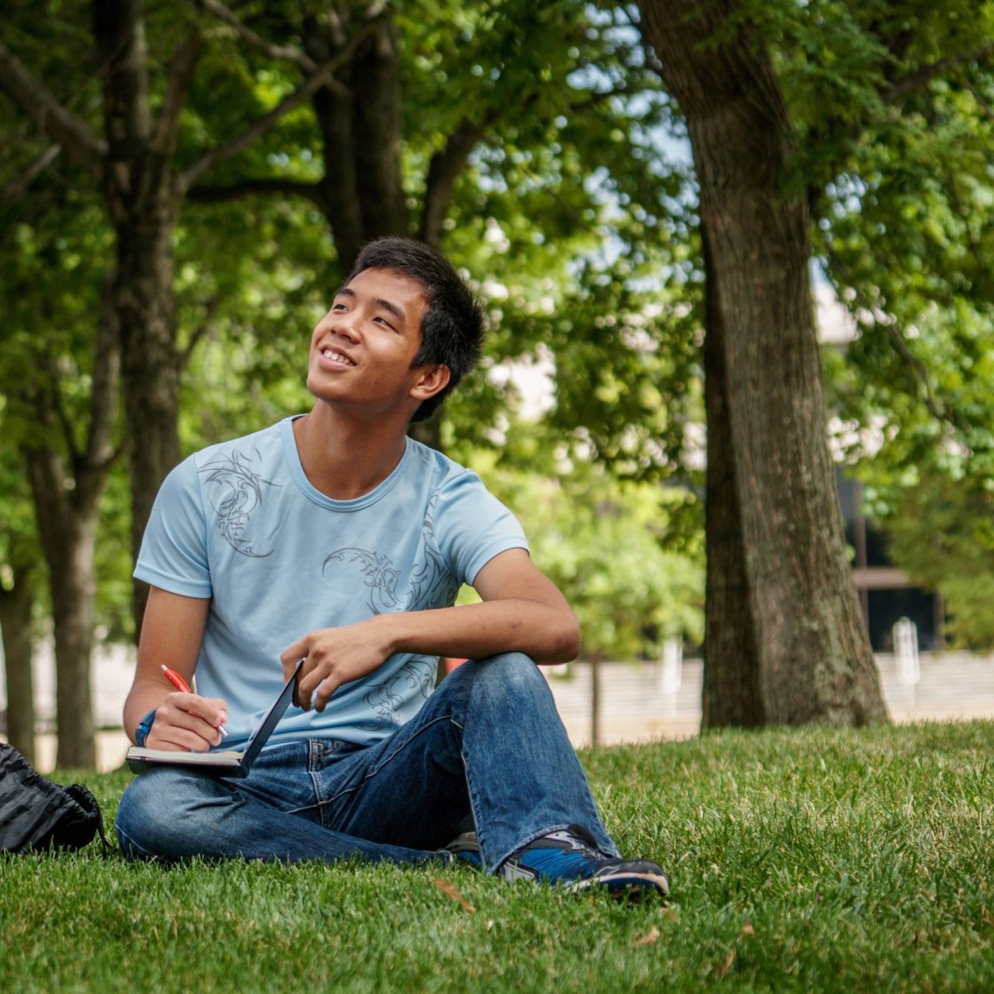 A college student sits in a grassy field and focuses his attention to the sky