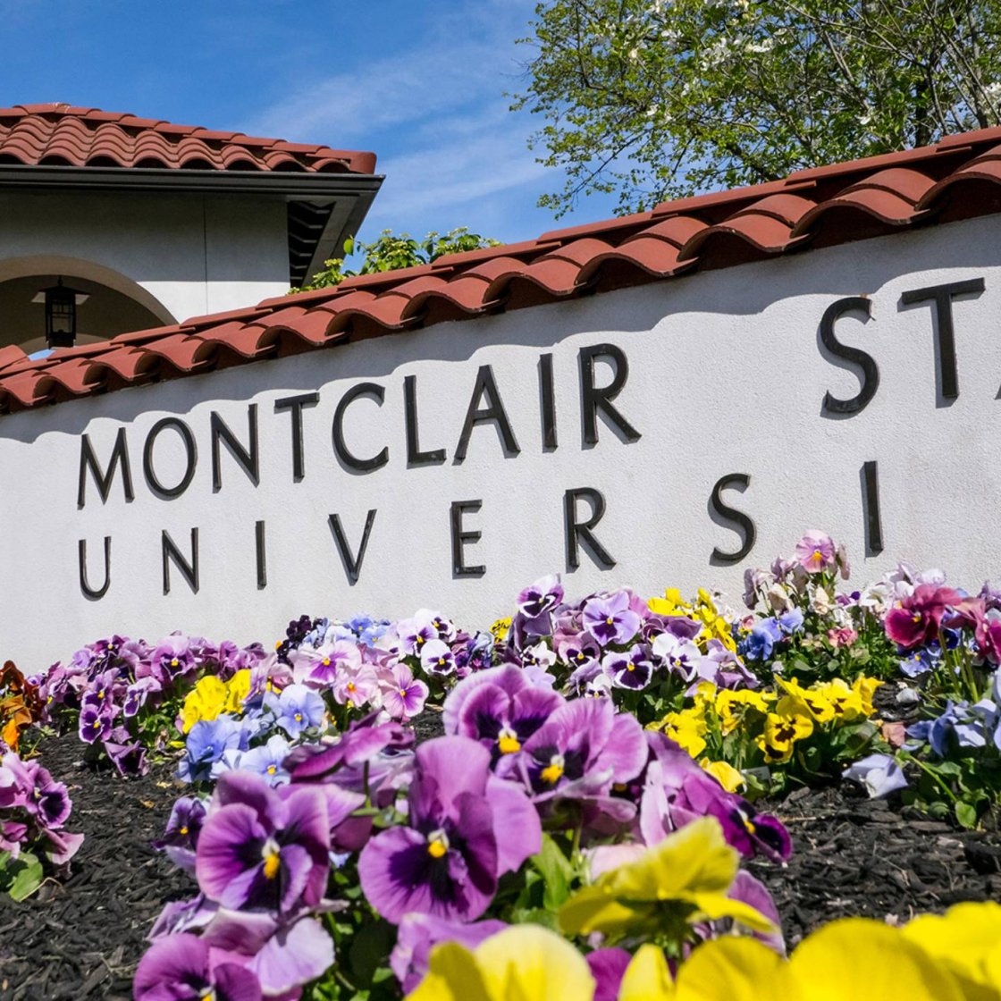 An exterior sign for Montclair State University with a bed of flowers in front of it