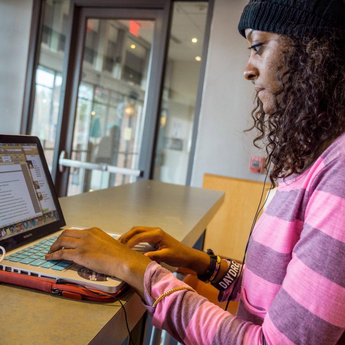 A college student sits at a table and types on a laptop