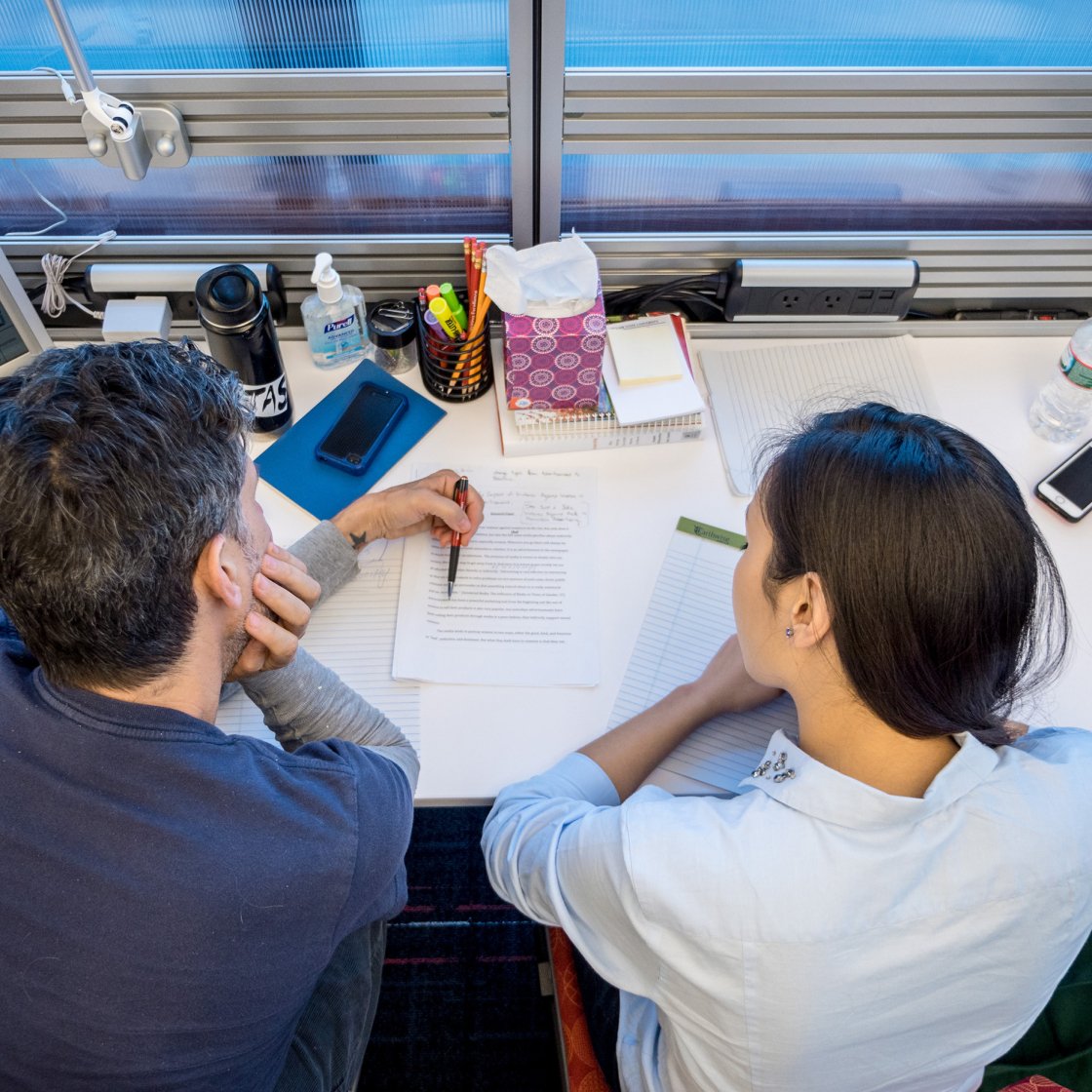writing consultation session with student and faculty at a desk reading and reviewing a paper
