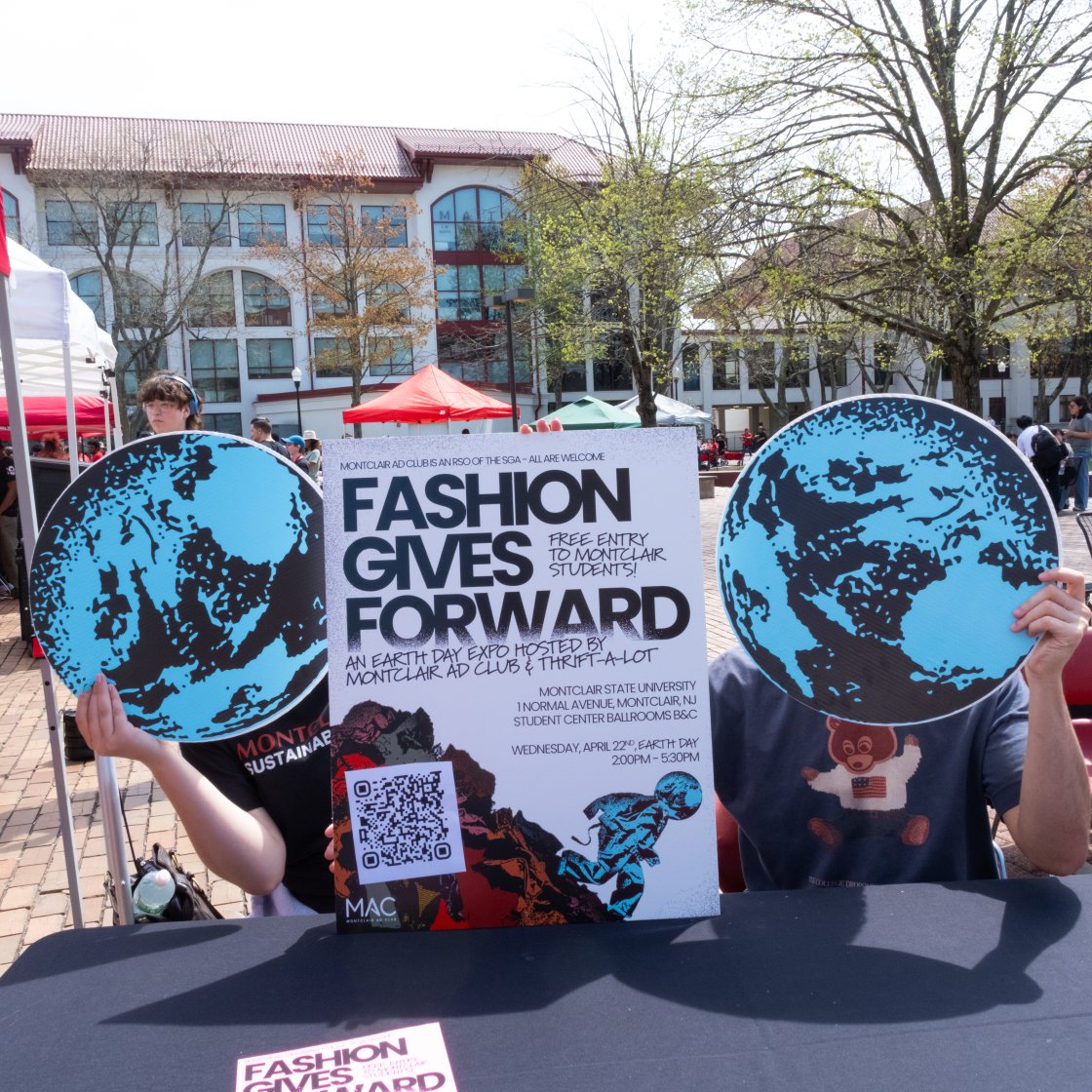 Students holding up a Fashion Gives Forward poster with two globe cutouts on each side.