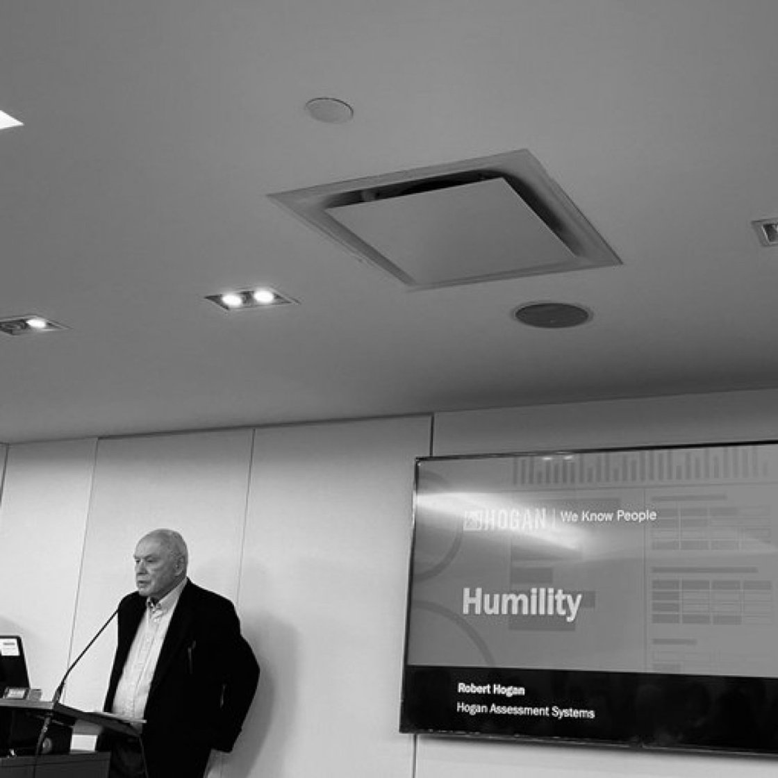 A black and white photo of an older man standing at a podium beside a large video screen