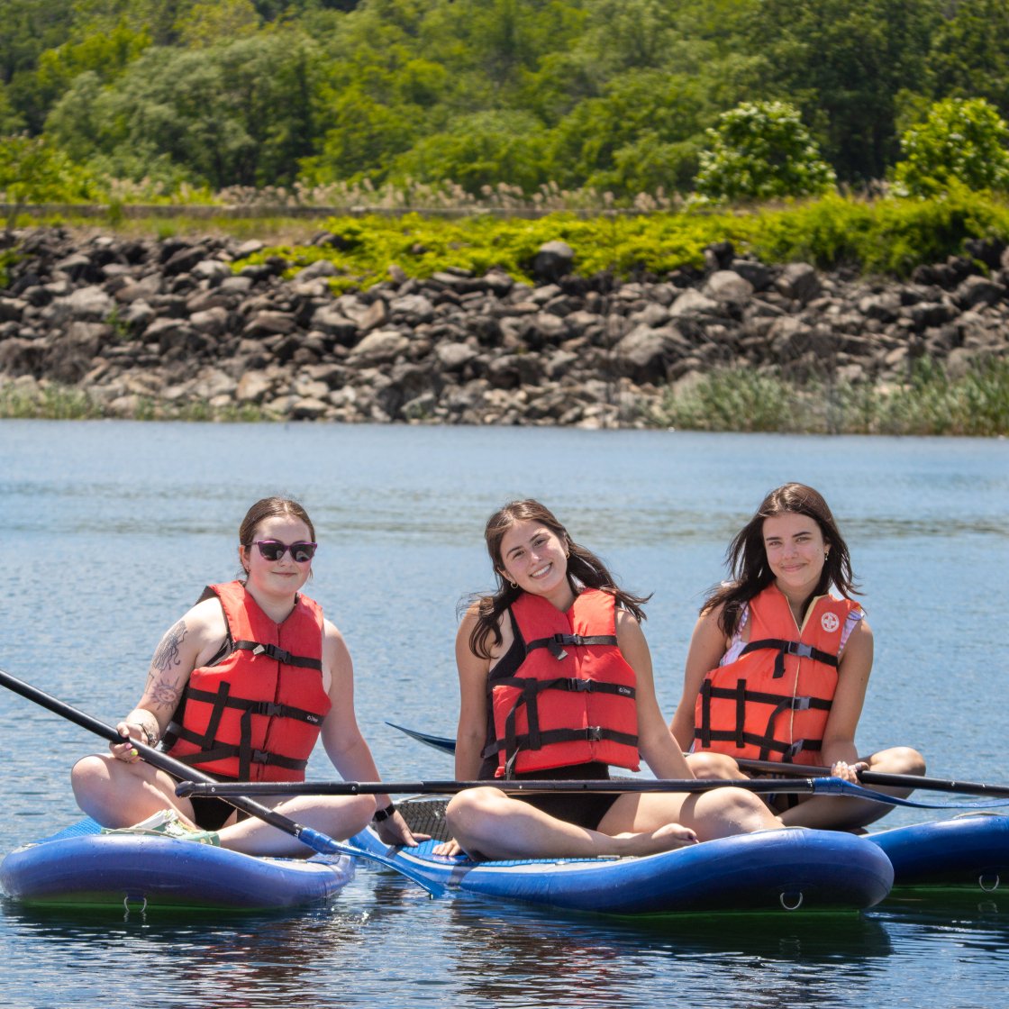 three students sitting on paddleboards in the middle of a lake