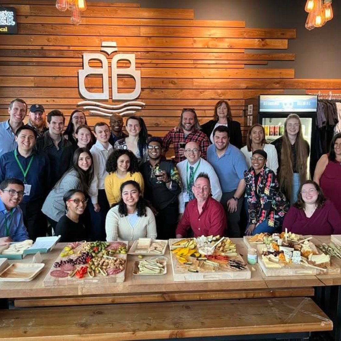 A large group of people in behind a wooden table displaying a variety of food