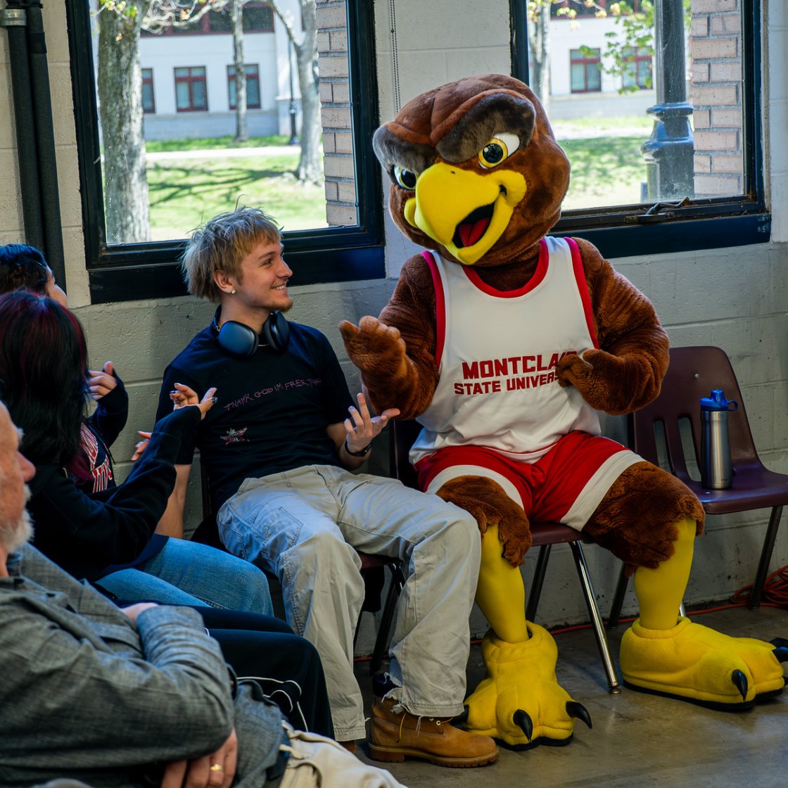 Rocky the Red Hawk, Montclair State University's mascot, sits with students in a group discussion during a campus outreach workshop.