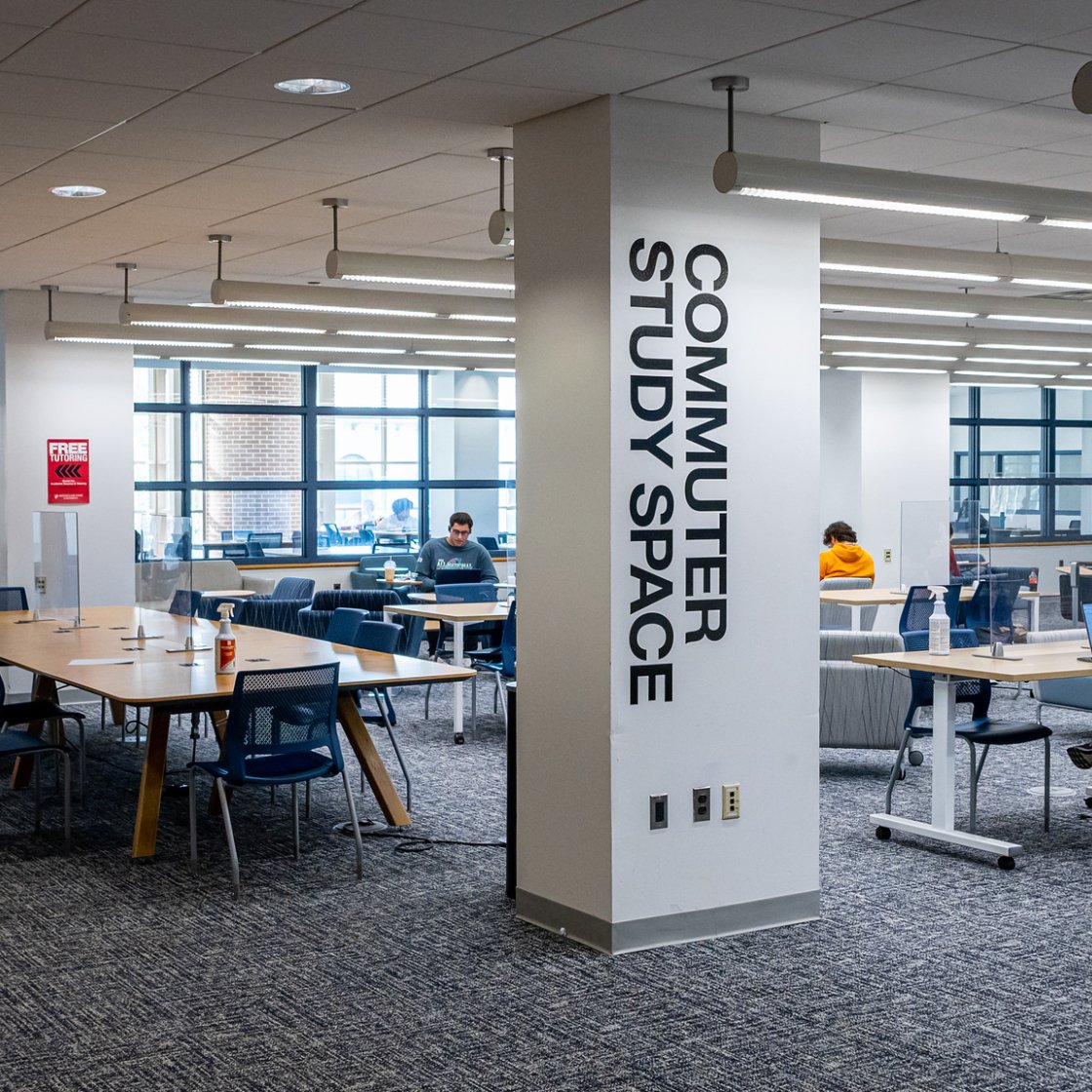 Students work independently at tables and lounge seating in a bright commuter study space with open seating and large windows.