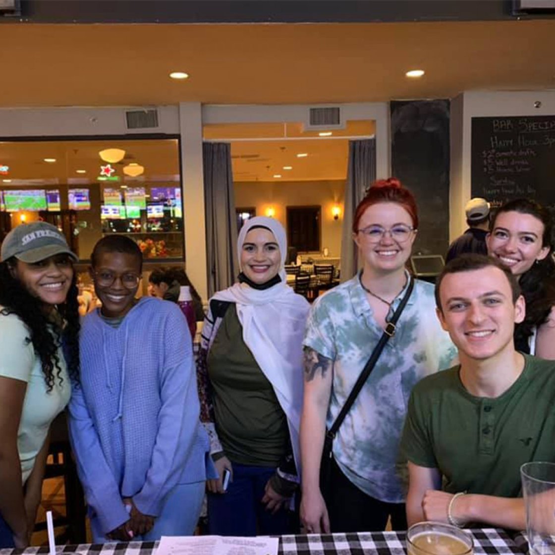 A group of six college students pose behind a table in a restaurant