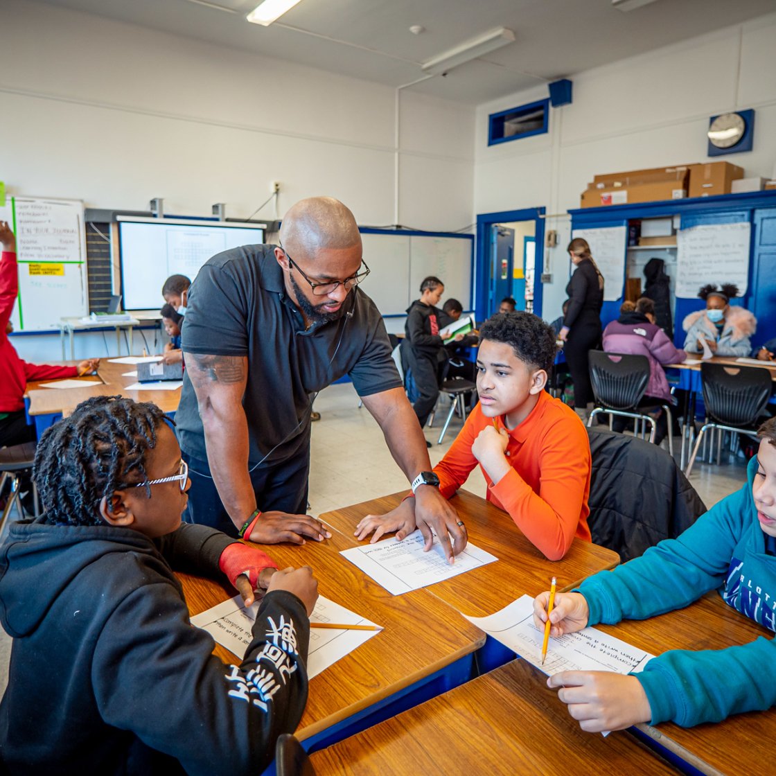 a teacher helps three boys at their desks