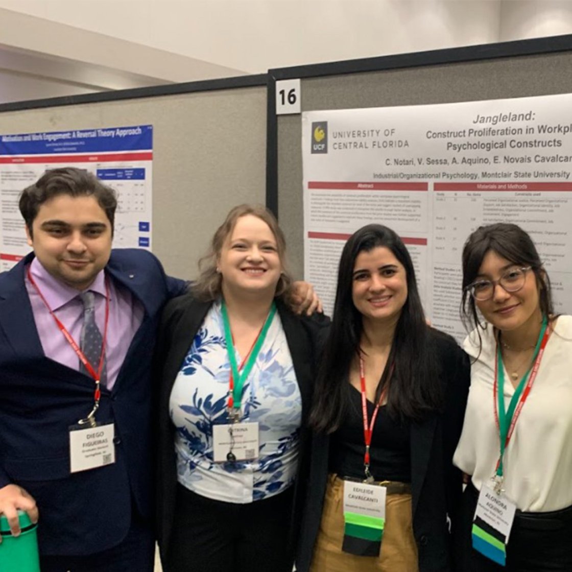 Four college students pose in a line in front of a printed presentation display 