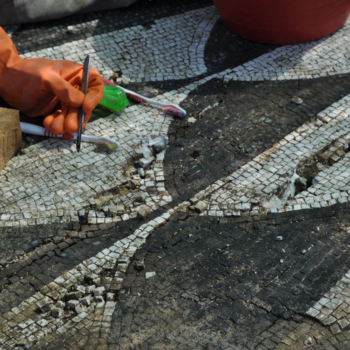 A hand holds a metal tool to clean a tile mosaic at an ancient Italian villa