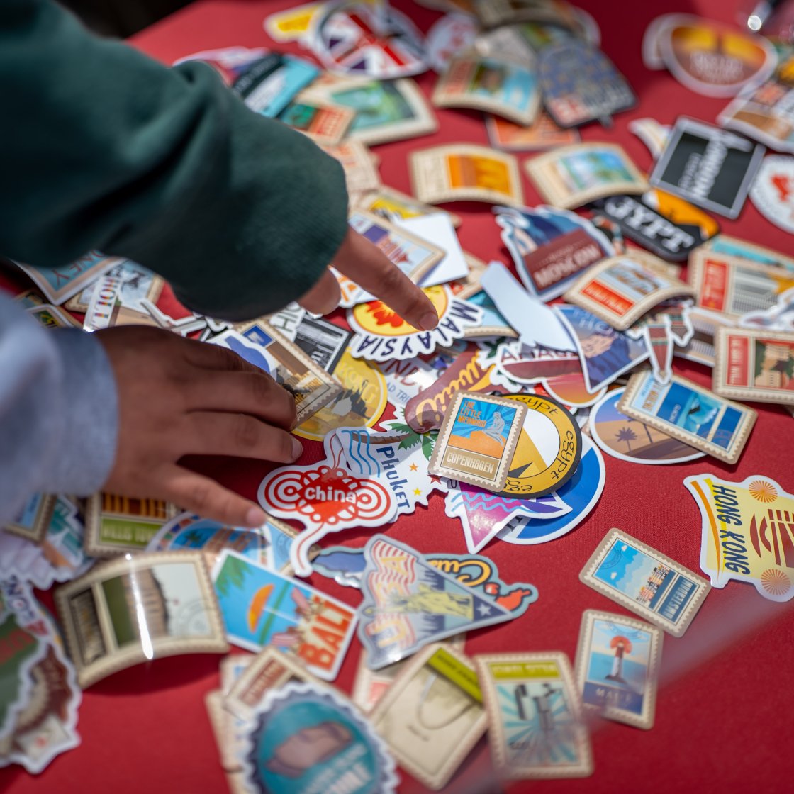 hands reaching to a table filled with stickers featuring international destinations