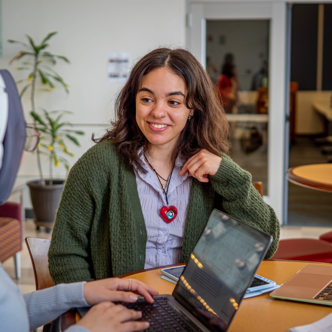 Two students talking, one on a laptop