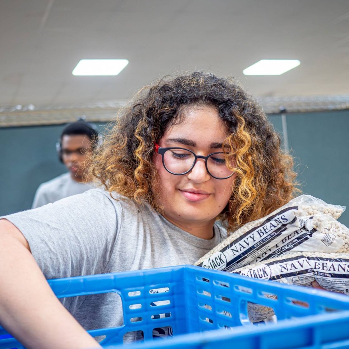 A woman pulls bags of navy beans out of a crate