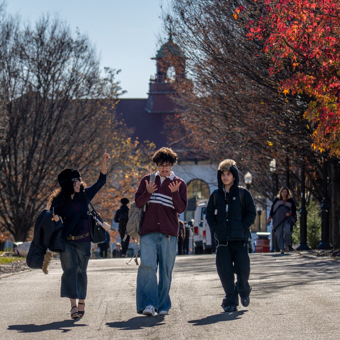 three students walking on campus, cole hall behind them