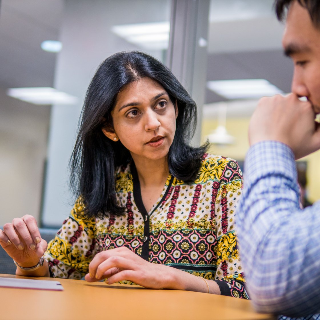 A student and professor discuss coursework across a table.