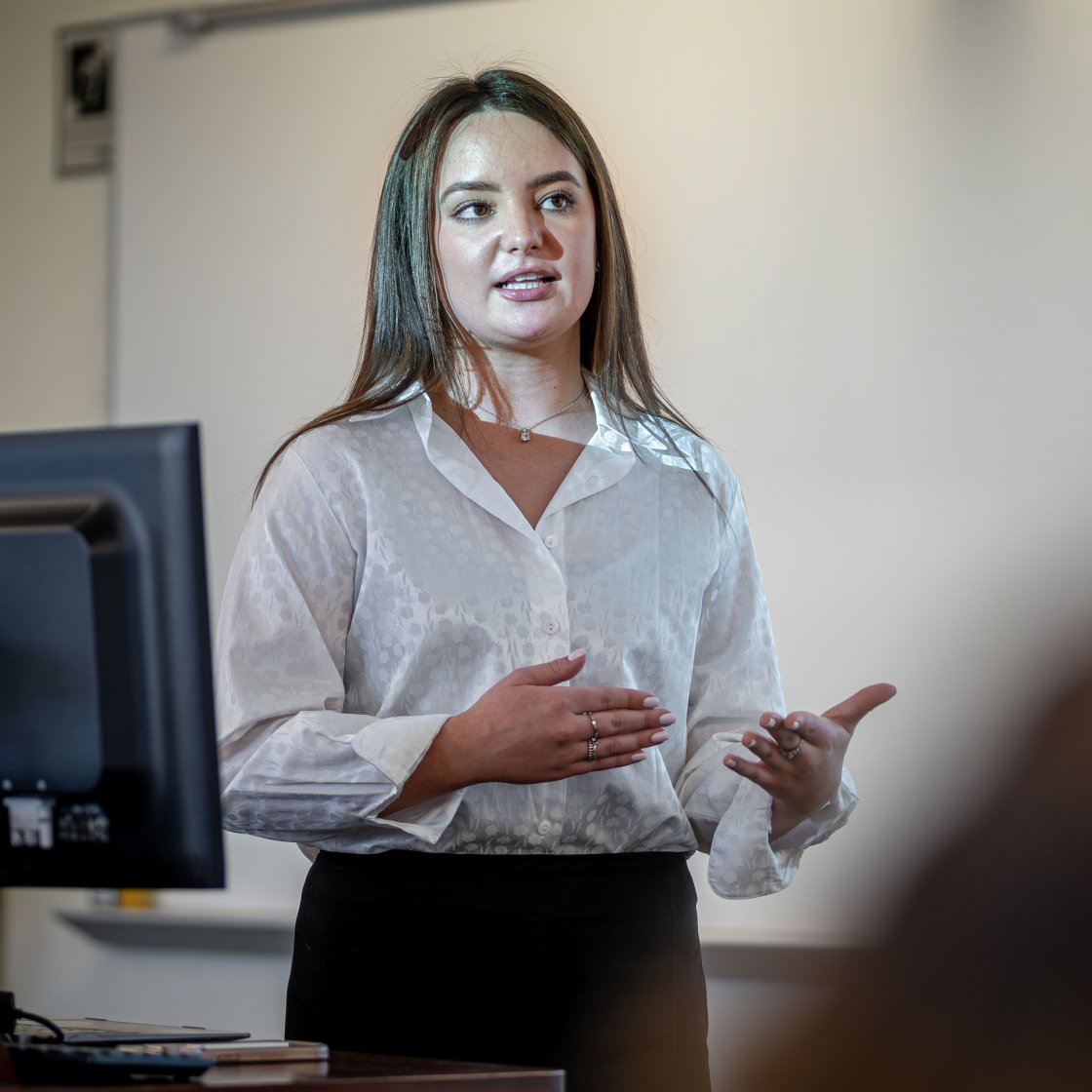 Student speaks beside a computer monitor during a presentation.