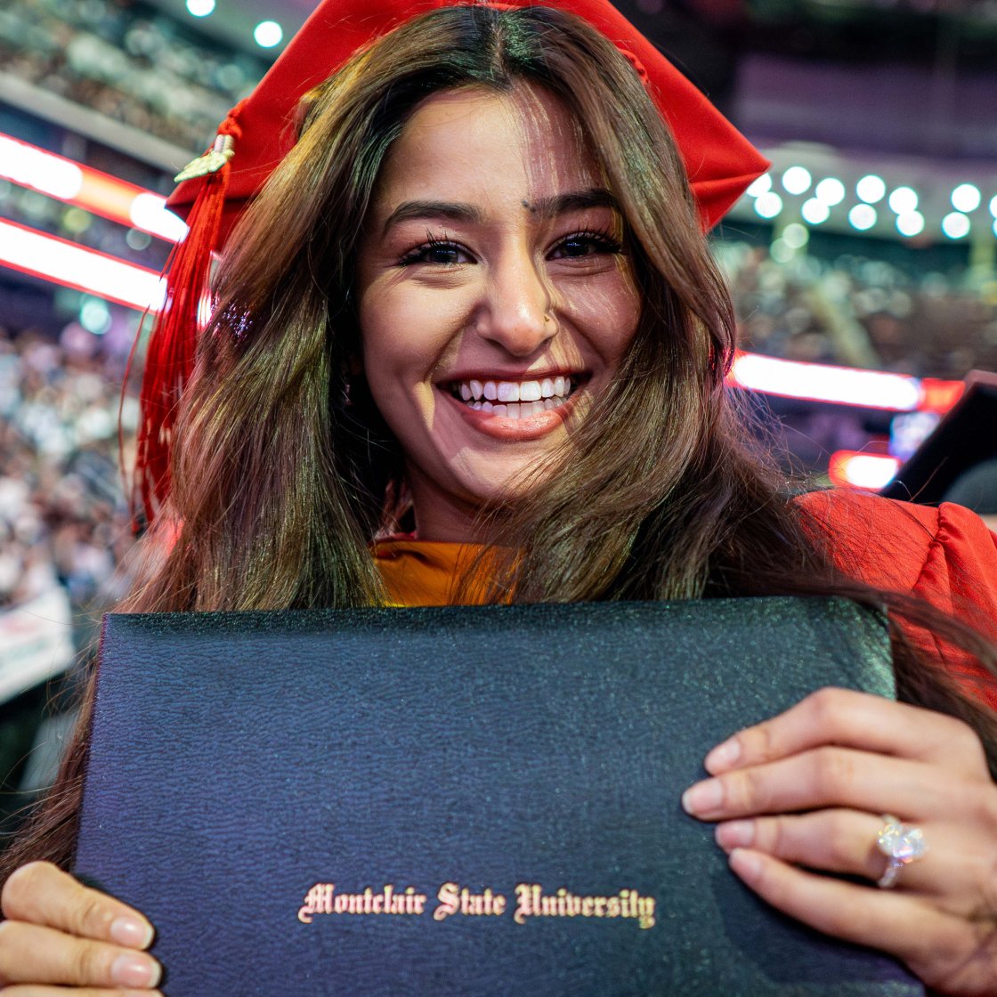 Graduate student smiles while holding her diploma at commencement.