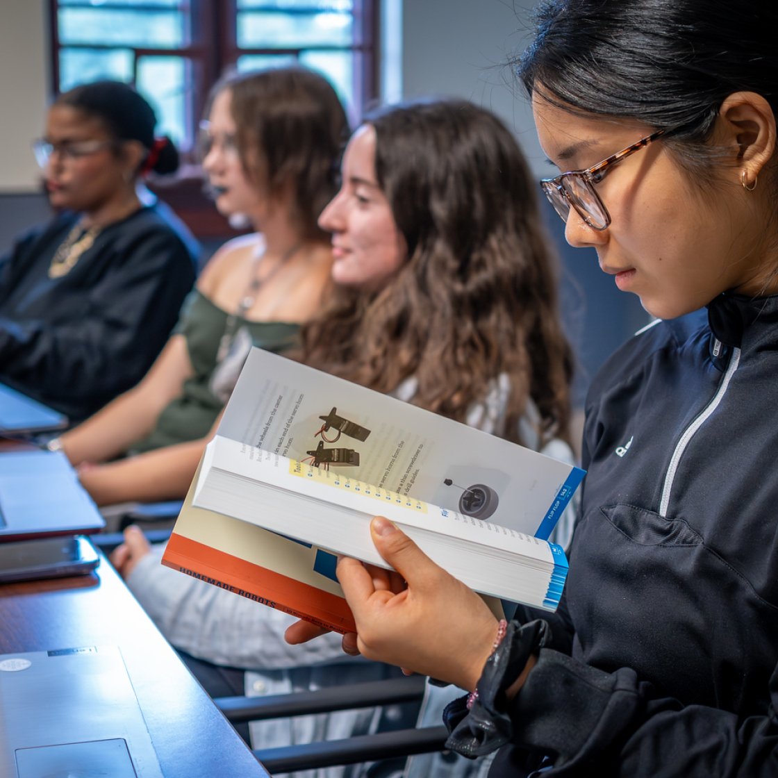 Student reading a book in class alongside peers.