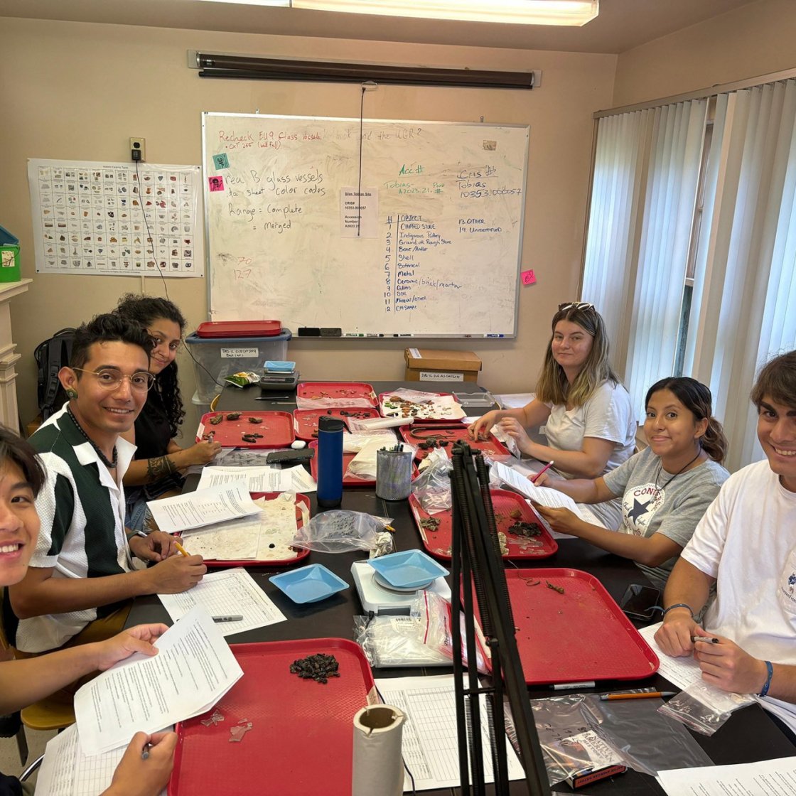A group of college students sit around sit around a table with trays and paperwork 