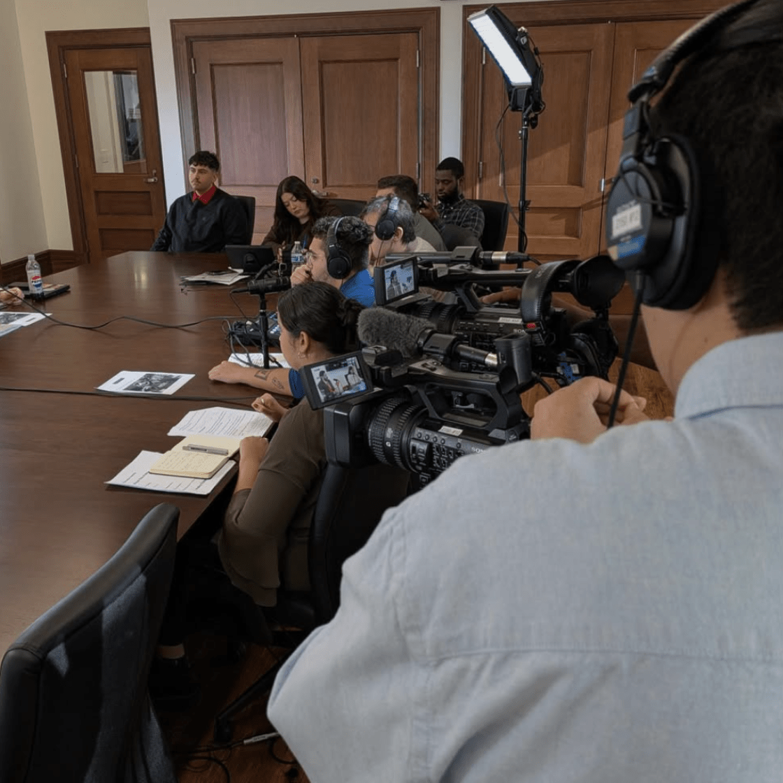 Student reporters sitting at long wooden table interviewing the president.