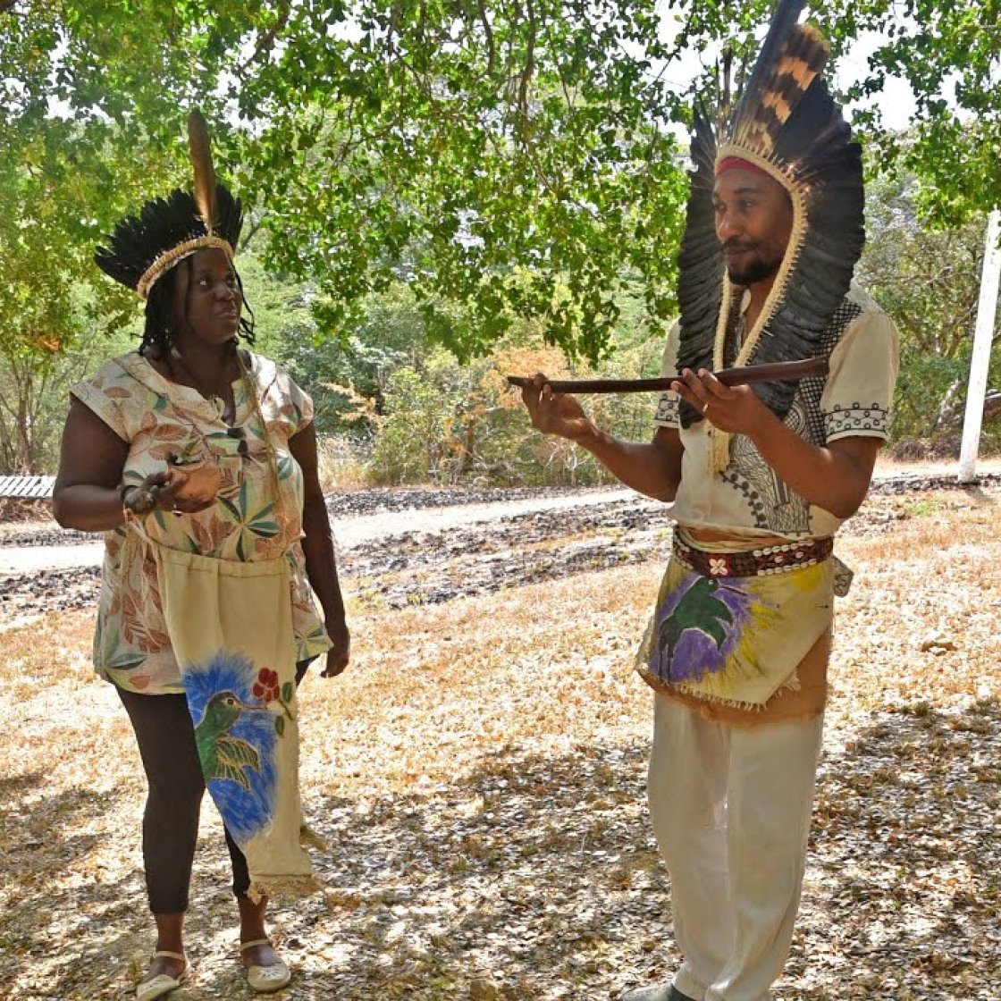 Two people wearing feathered ceremonial attire with ceremonial objects