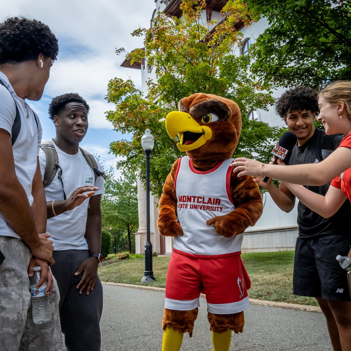 Students interview Rocky the Red Hawk on a campus walkway during a Weeks of Welcome activity.
