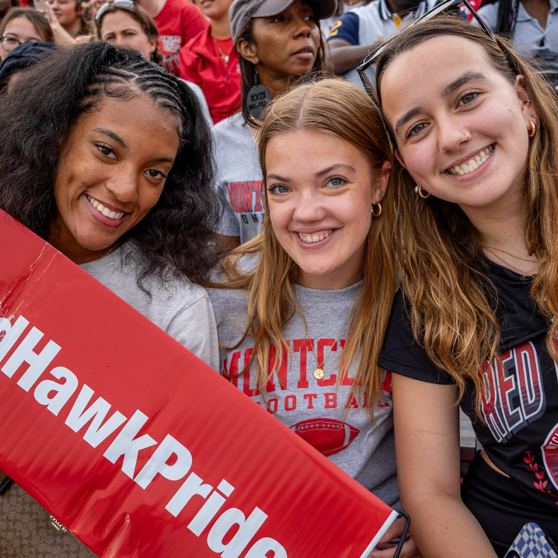 Three students smiling holding a #RedHawkPride banner. 