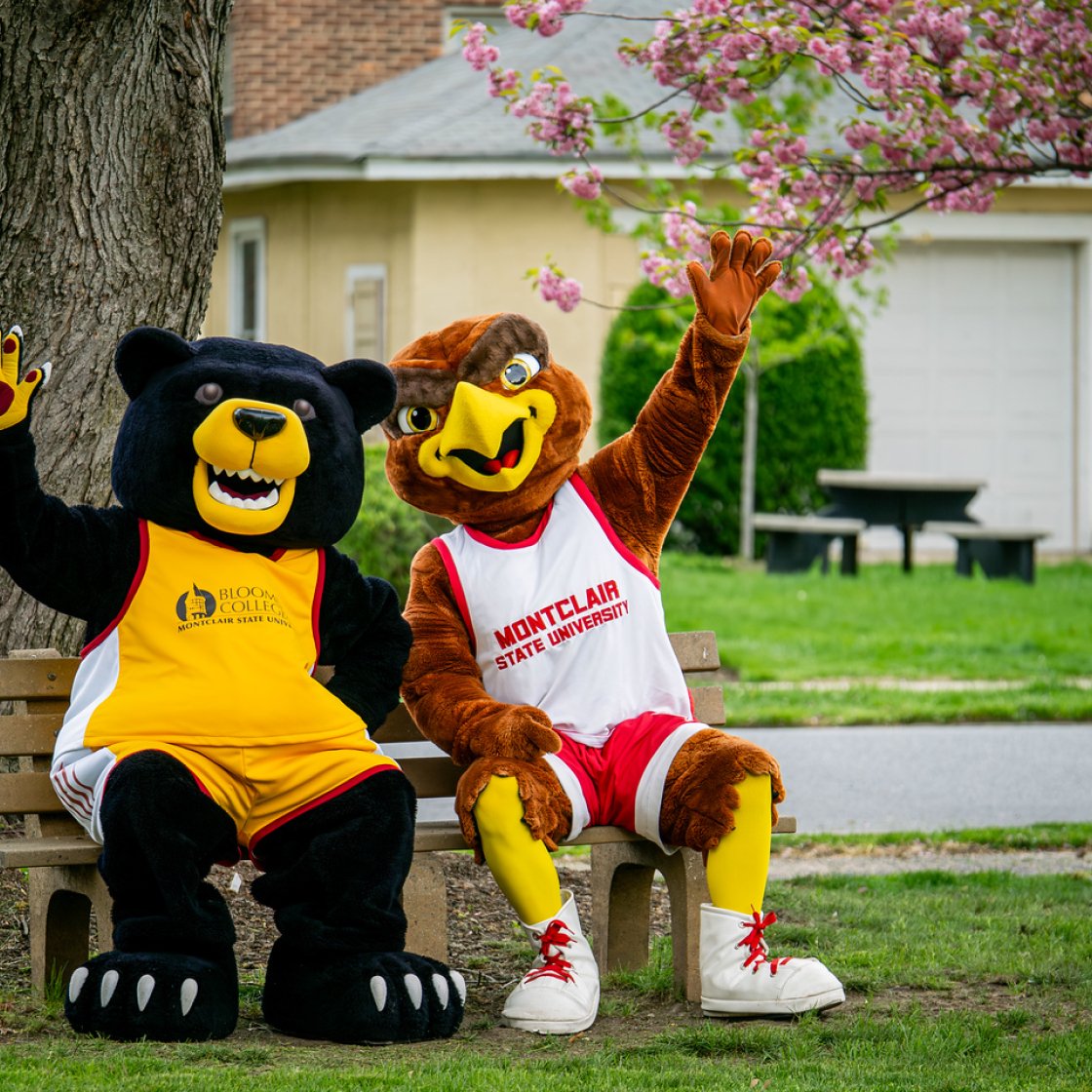 Deacon the Bloomfield Bear and Rocky the Red Hawk Mascots sitting on a bench waving 