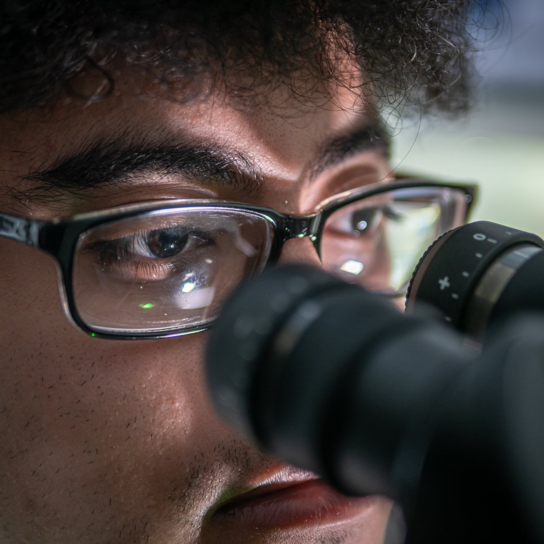 A person with glasses looking into a microscope