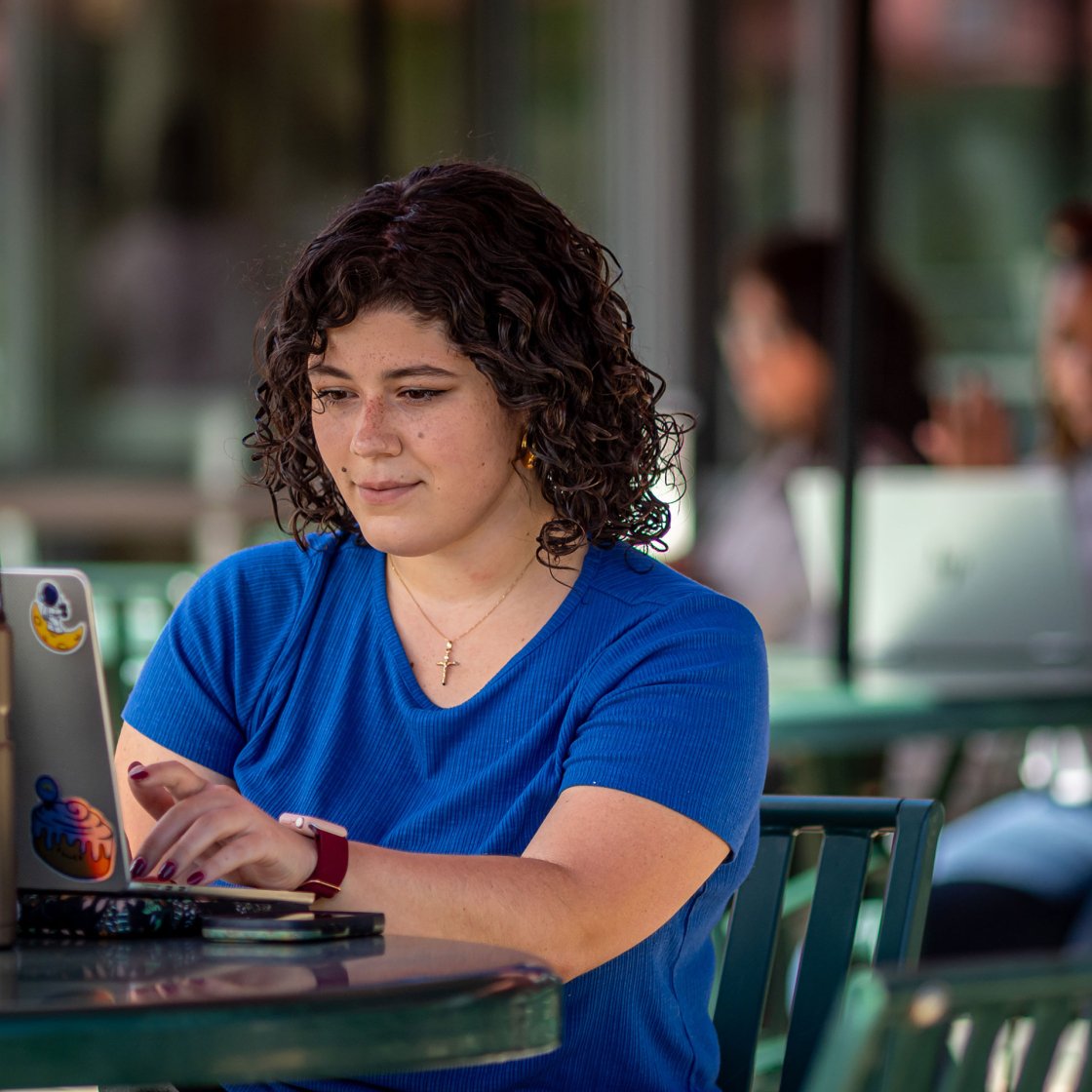 Student working on their laptop outside in a cafe patio.