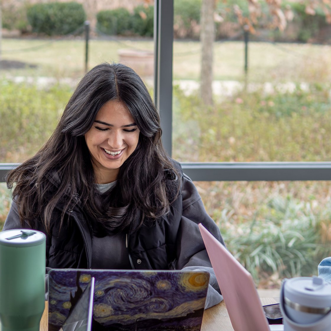Student working on their laptop in a cafe and smiling.