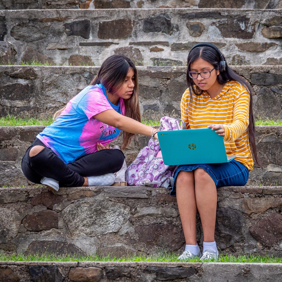 Two students sitting on stairs looking at a laptop together.
