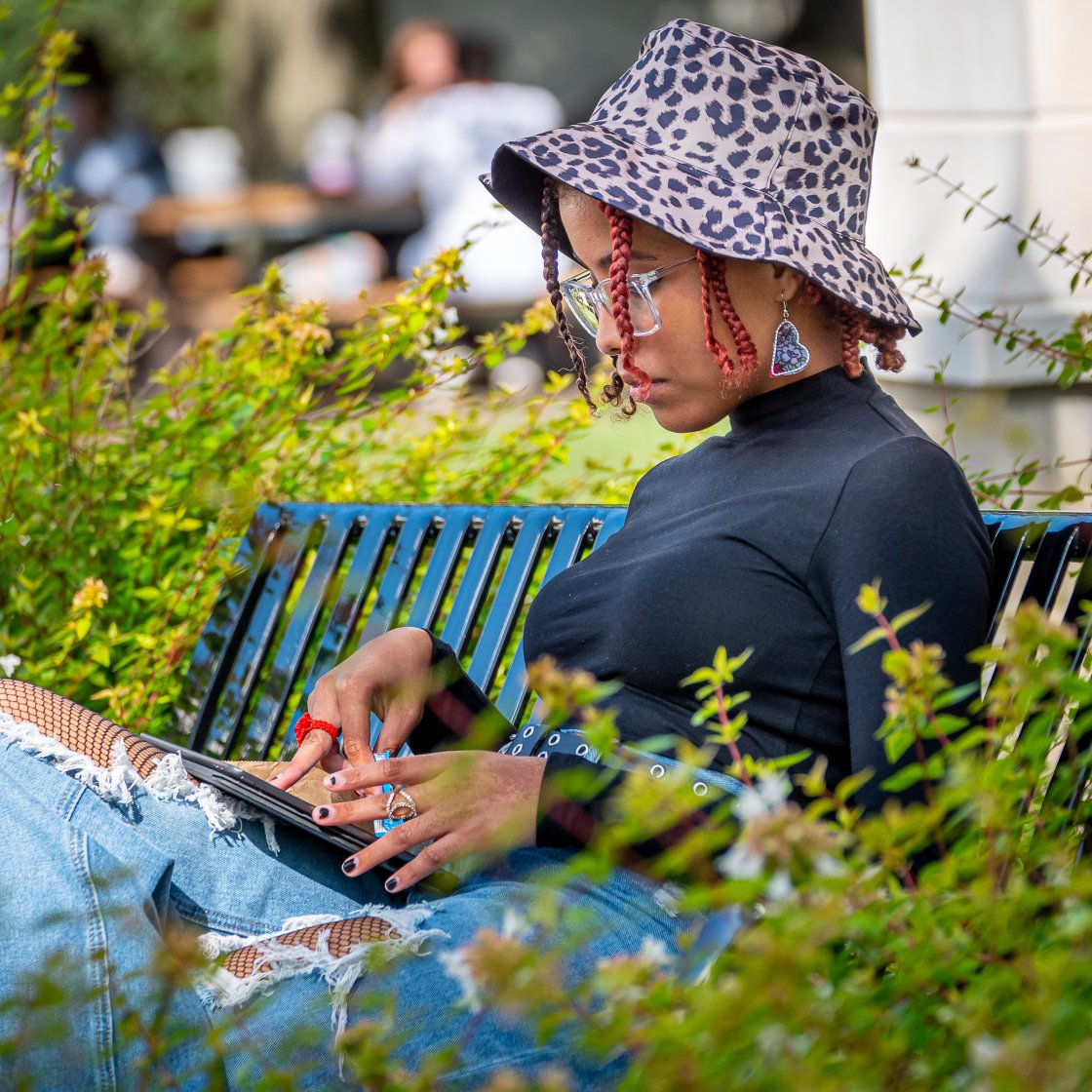 A student sitting on a bench looking at their electronic device.